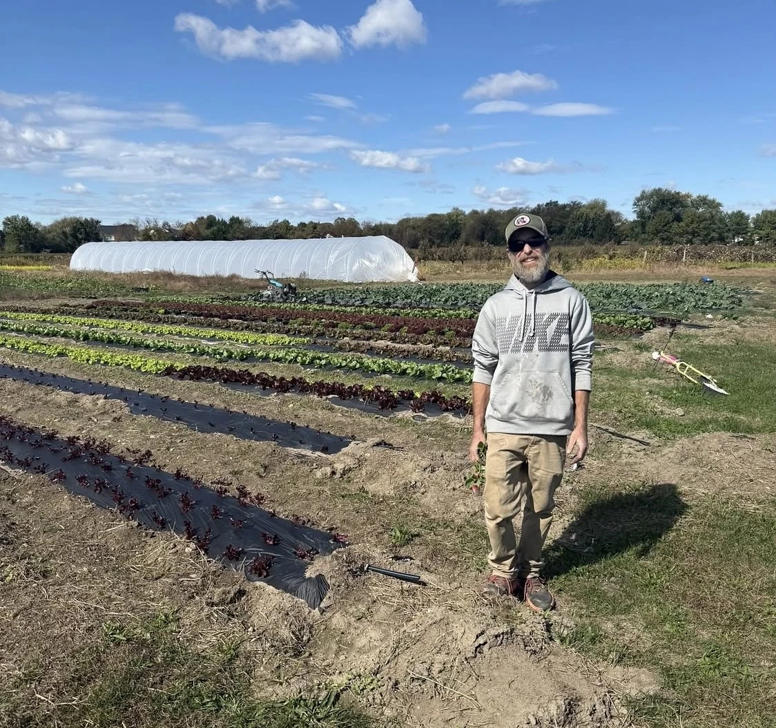 A grower standing among growing beds beside a greenhouse
