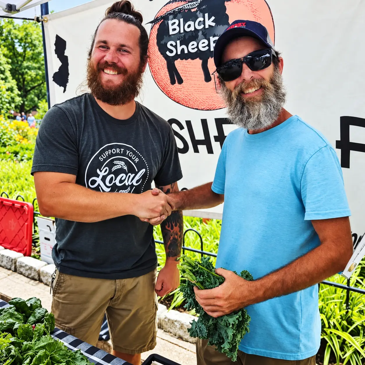 Two growers shaking hands in front of the Black Sheep Farm banner, one holding fresh kale